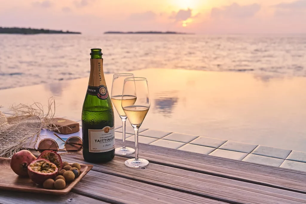 Bottle of champagne with glasses and snacks at sunset by the private pool in the villa